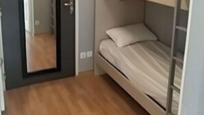 Una habitación pequeña con cama individual, piso de madera, una puerta y un espejo en la pared.
