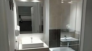 Un baño moderno con un lavabo blanco, una ducha con mampara de vidrio y un espejo sobre el lavabo.