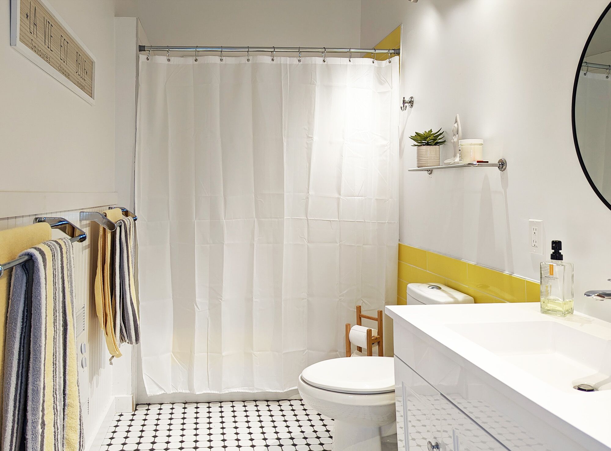 Ein Badezimmer mit Duschvorhang, Toilette, Waschbecken mit Spiegel und Ablage für Toilettenartikel.
