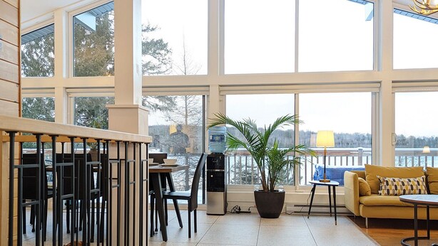 Tilava sisätila, jossa on suuret ikkunat, kattotuuletin, puinen penkki, sohva, pöytä ja ruukussa oleva kasvi.