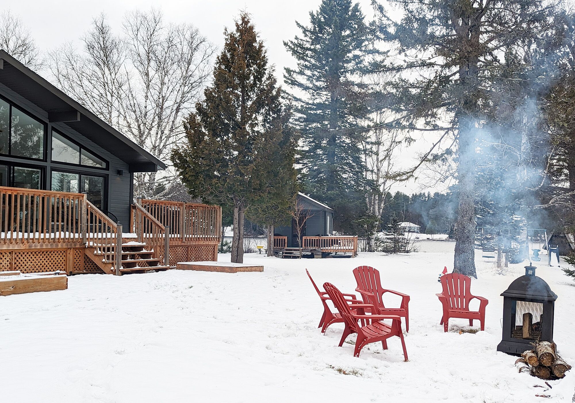 A modern cabin with a wooden deck, red Adirondack chairs, and a log fire.