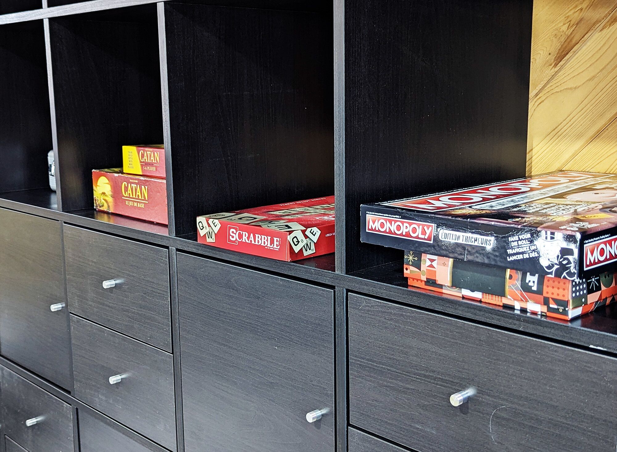 A storage unit with drawers and shelves containing board games like Scrabble, Catan, and Monopoly.