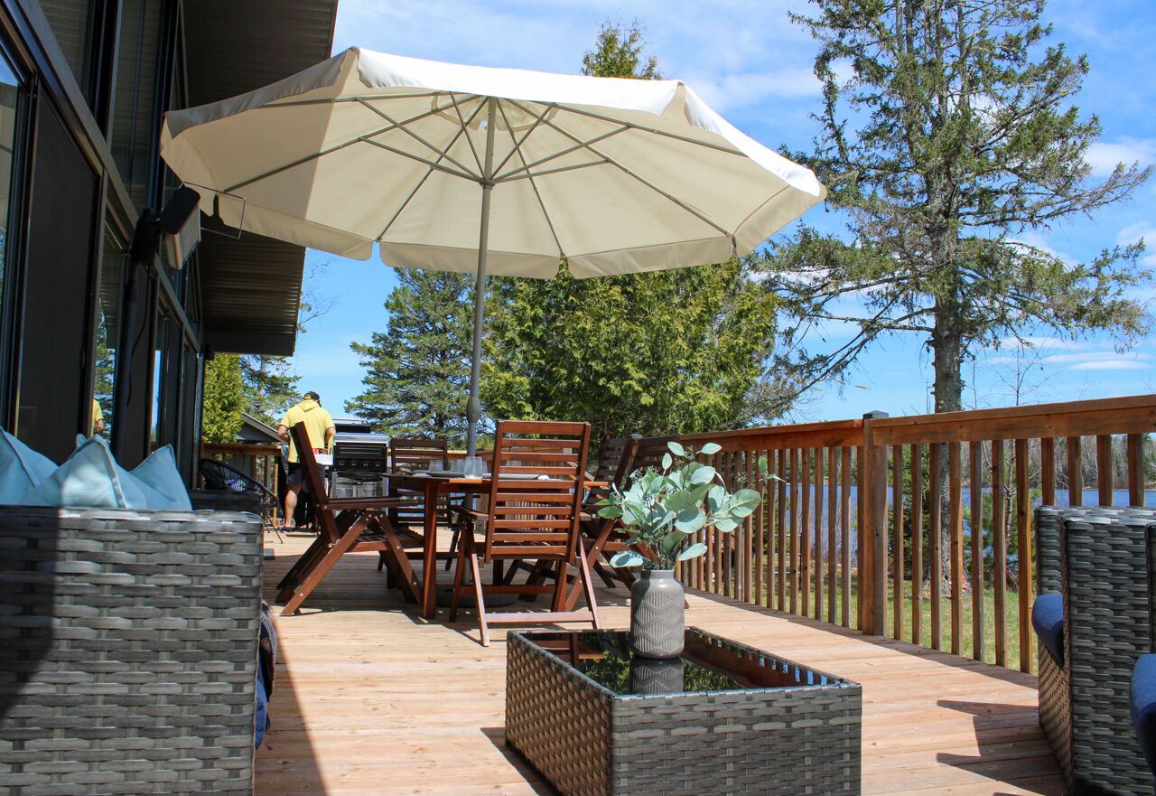 Eine Terrasse im Freien mit Tisch, Stühlen und einem großen Sonnenschirm, sowie einem Holzzaun.