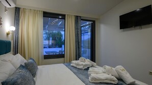 A hotel room with a bed, a flat-screen TV, a window with curtains, and a view of the outdoors.