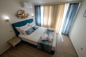 A modern bedroom with a large bed, a bedside table, a wall-mounted air conditioner, and a decorative wall piece. - Apartment with Sea View (Kalamata)