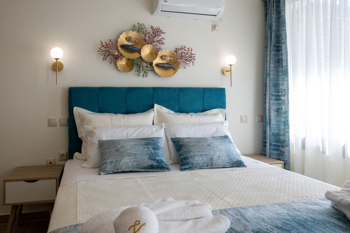A neatly made bed with a teal headboard, white and blue pillows, and a decorative wall piece above it.