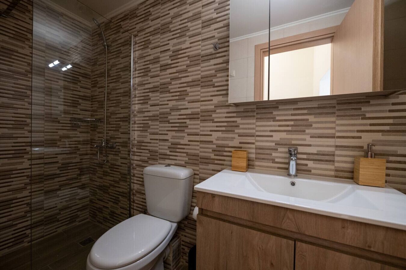 A modern bathroom with a glass shower enclosure, a toilet, and a vanity with a sink and mirror.