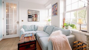 Een woonkamer met een lichtblauwe modulaire bank, een houten salontafel, een spiegel en een raam met uitzicht op bomen.