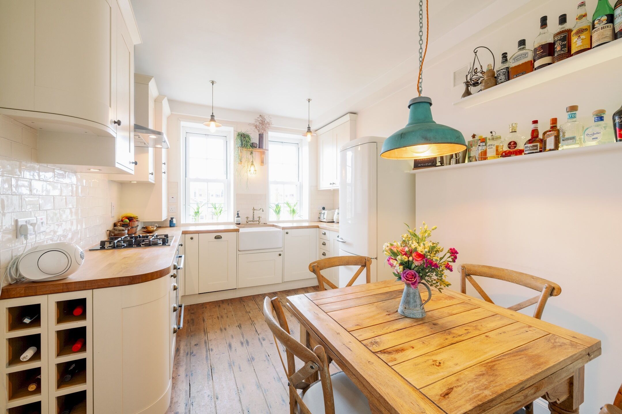 Een keuken met witte kasten, een houten eettafel en een hangende lamp.
