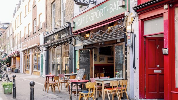Een straat met terrasjes van een café genaamd 'Cafe Sport Bar'.