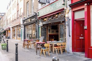 Une rue où l’on trouve un café appelé « Café Sport Bar » et qui dispose de tables en terrasse.