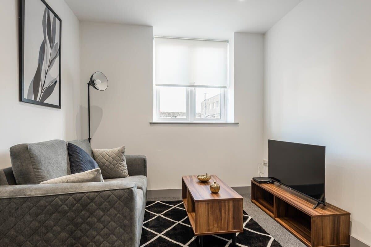 A modern living room with a grey sofa, a wooden coffee table, a flat-screen TV on a wooden stand, and a floor lamp.