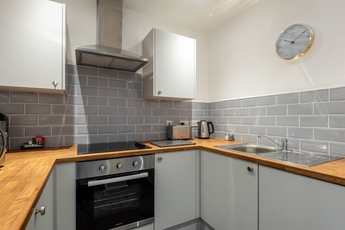 A compact kitchen with grey tiled backsplash, stainless steel appliances, and a wooden countertop.