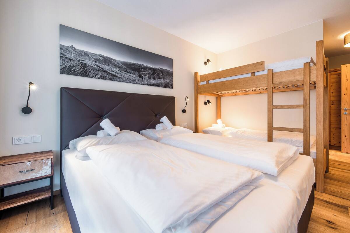 Habitación de hotel con dos camas, una litera de madera, un escritorio y un cuadro colgado en la pared.