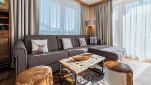 Ein modernes Wohnzimmer mit einer Eckcouch, einem Couchtisch aus Holz und einem großen Fenster mit Vorhängen.