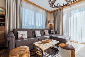 Un salon moderne avec un canapé d’angle, une table basse en bois et une grande fenêtre agrémentée de rideaux.