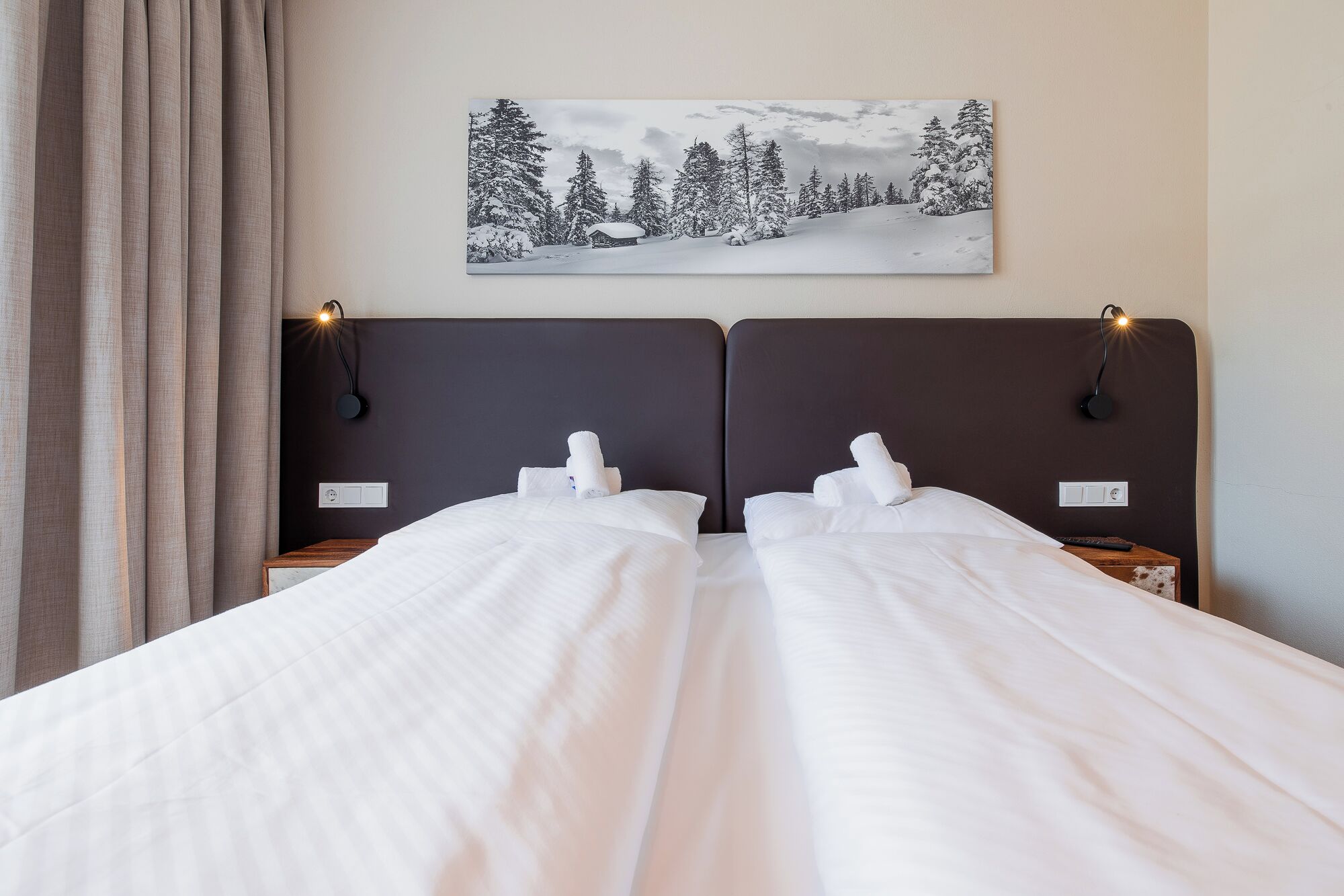 Ein Doppelbett mit weißer Bettwäsche, zwei Nachttische mit Lampen und ein Winterbild über dem Bett.