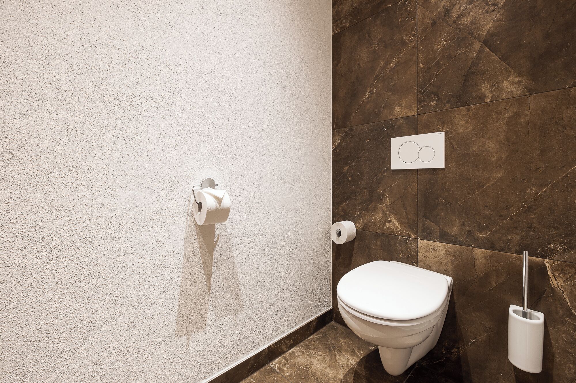 Ein Badezimmer mit Toilette, Papierhandtuchspender und Wandspülknopf.