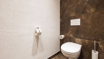 Ein Badezimmer mit Toilette, Papierhandtuchspender und Wandspülknopf.