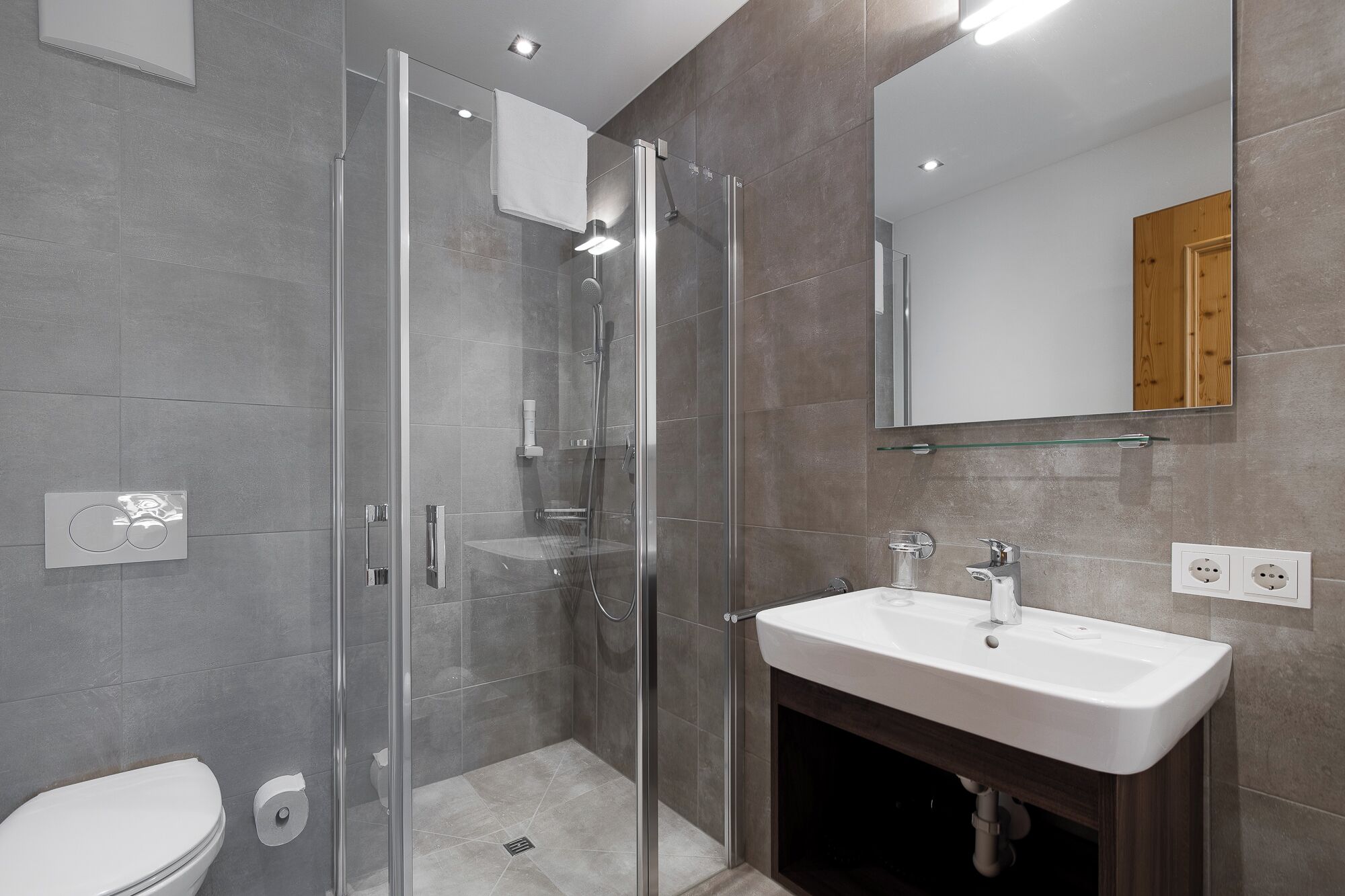 Een moderne badkamer met een douchecabine van glas, een witte wastafel en een grote spiegel.