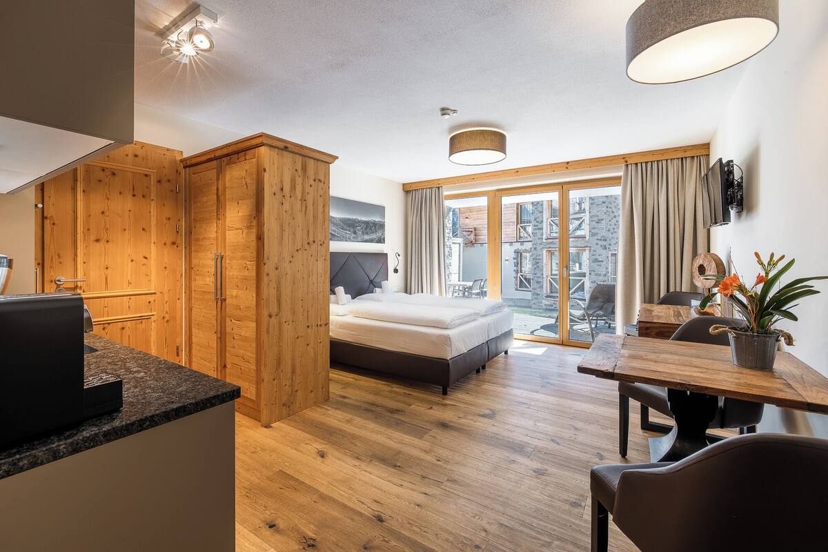 Habitación de hotel moderna con un armario de madera, una cama, una mesa de comedor y vistas al exterior.