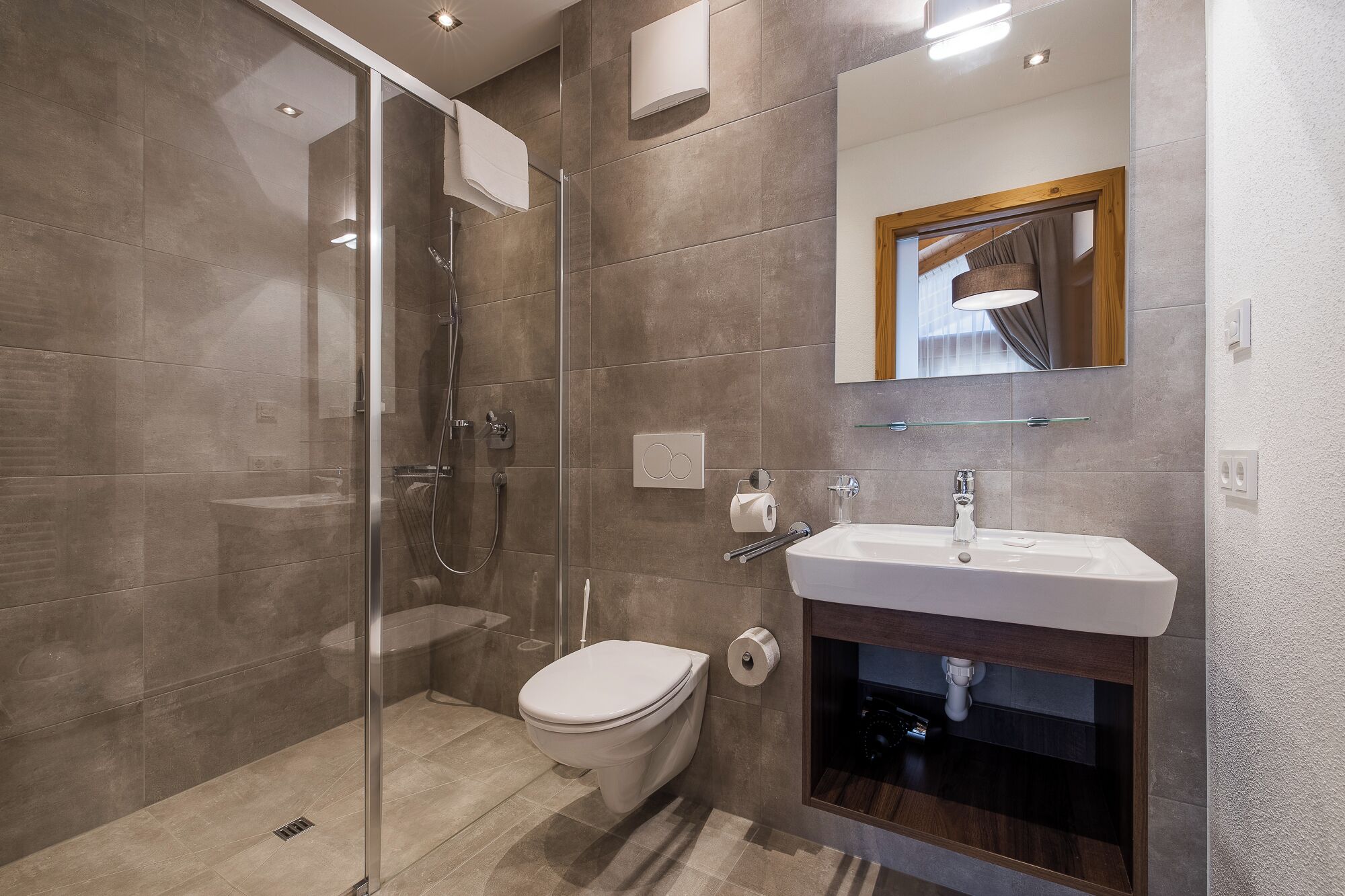 A modern bathroom with a glass shower enclosure, a toilet, a sink, and a mirror.