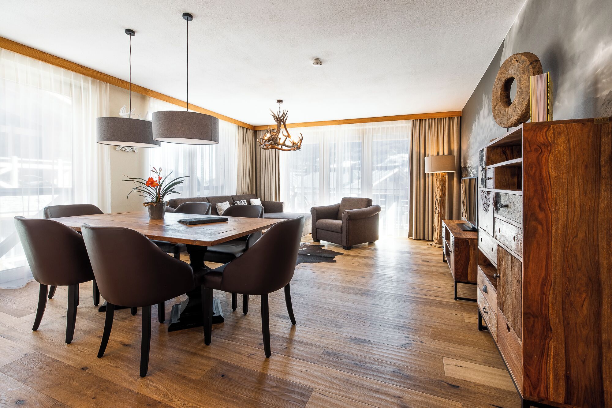 A modern dining area with a wooden table and chairs, a chandelier, and a wooden cabinet with drawers.