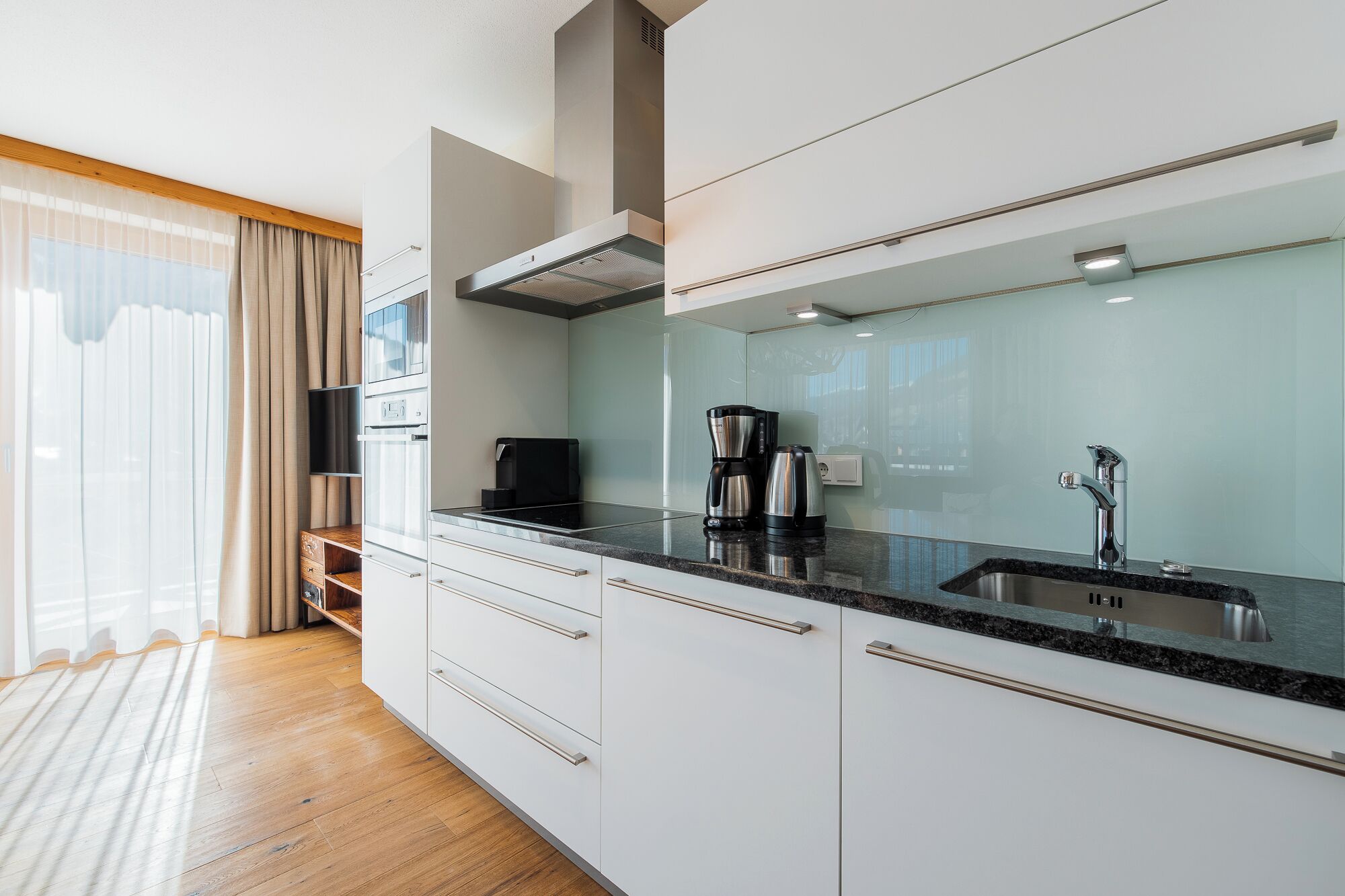 A modern kitchen with white cabinets, a black countertop, and a stainless steel sink.