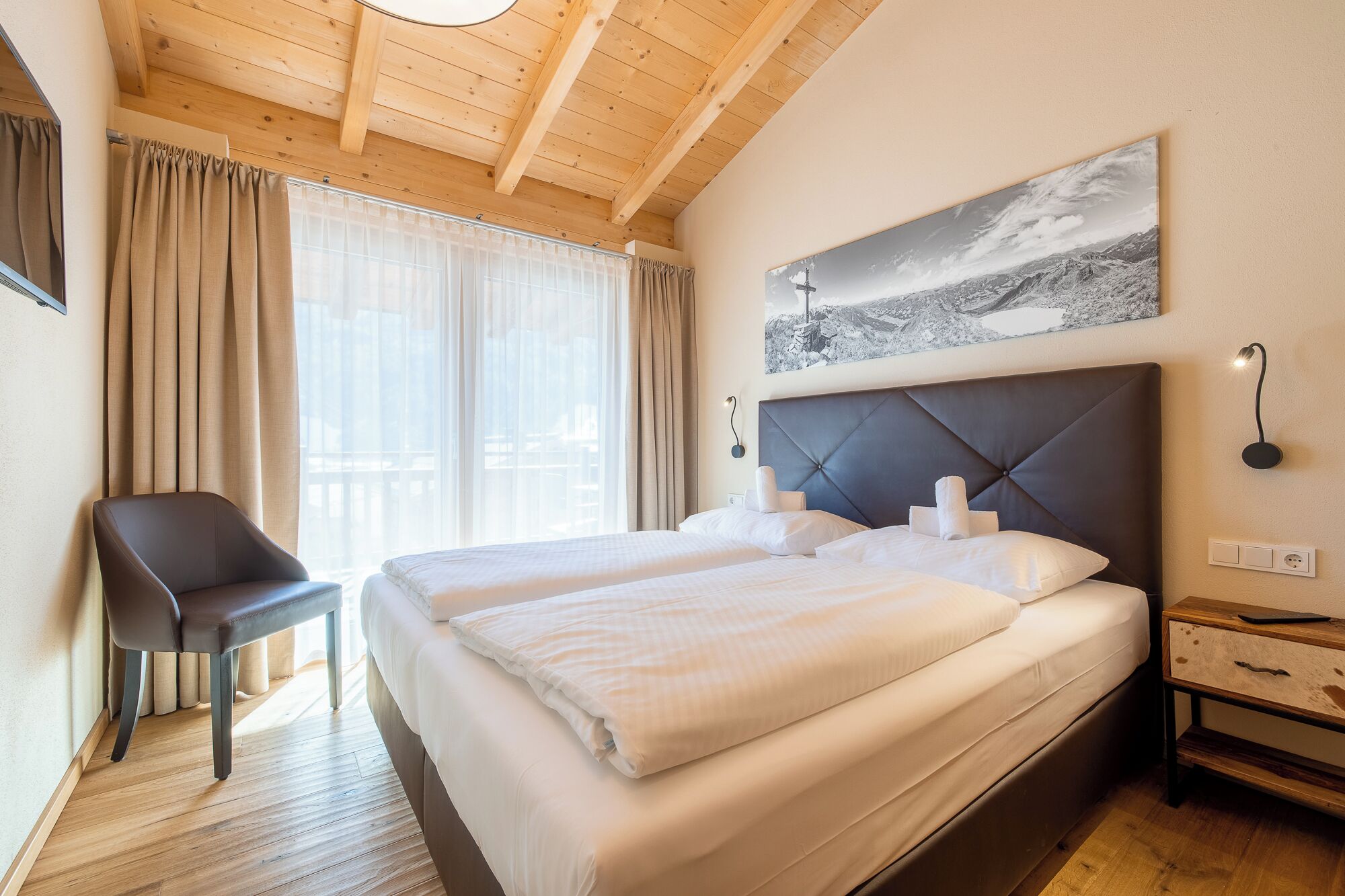 Habitación de hotel con una cama grande, una silla, una mesita de noche y una lámpara de pared.