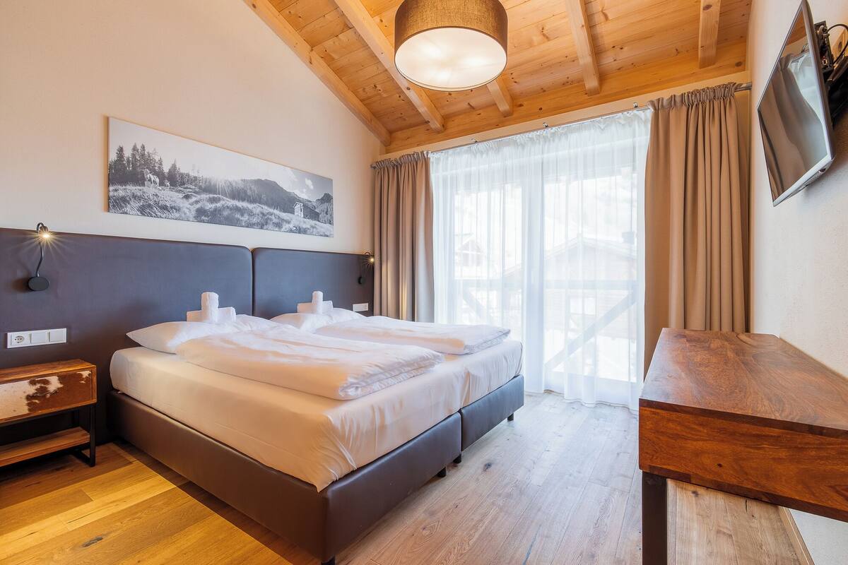 Un dormitorio con cama, un escritorio de madera, un televisor y una ventana con cortinas.