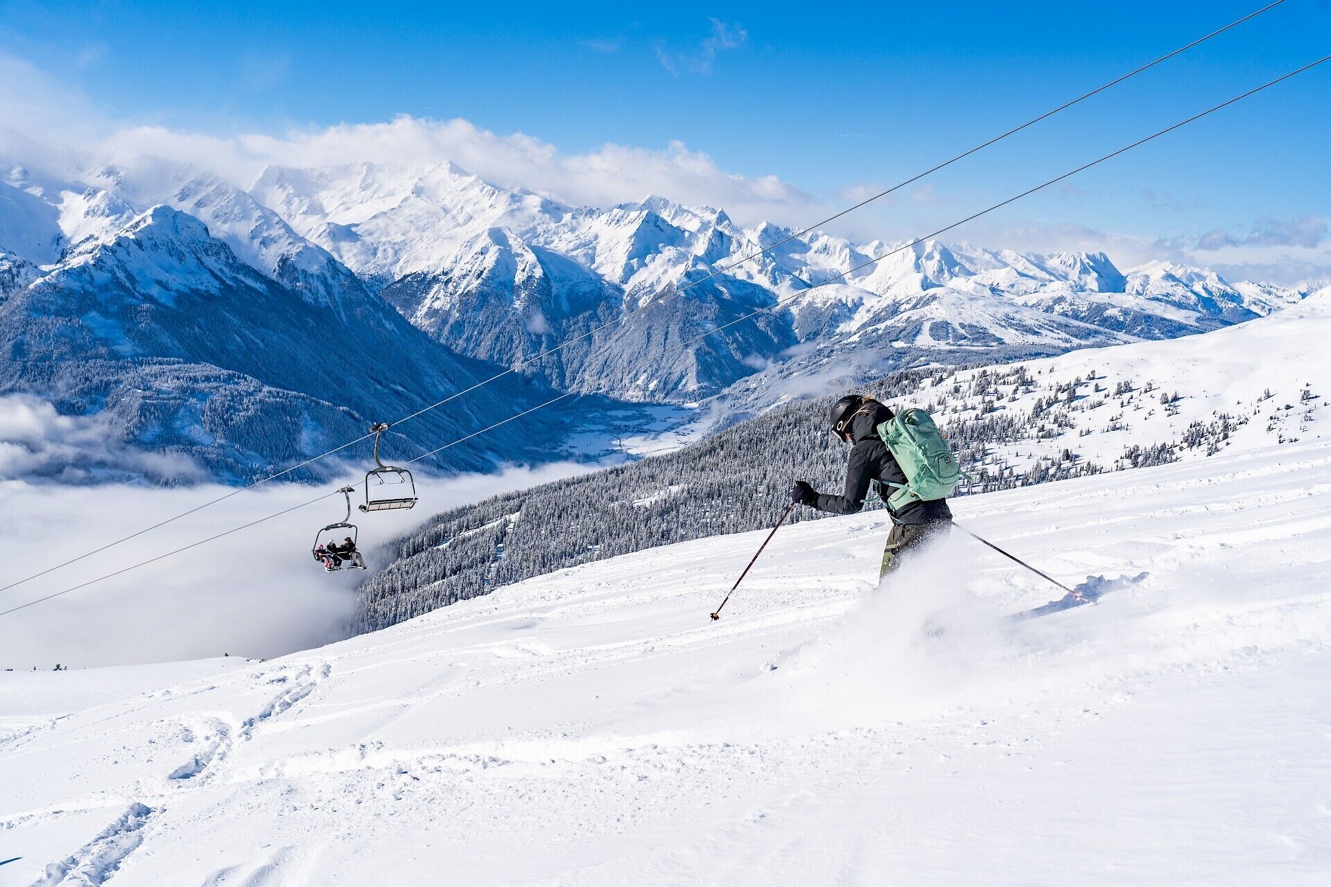 Une piste de ski avec un télésiège et un skieur en train de descendre.