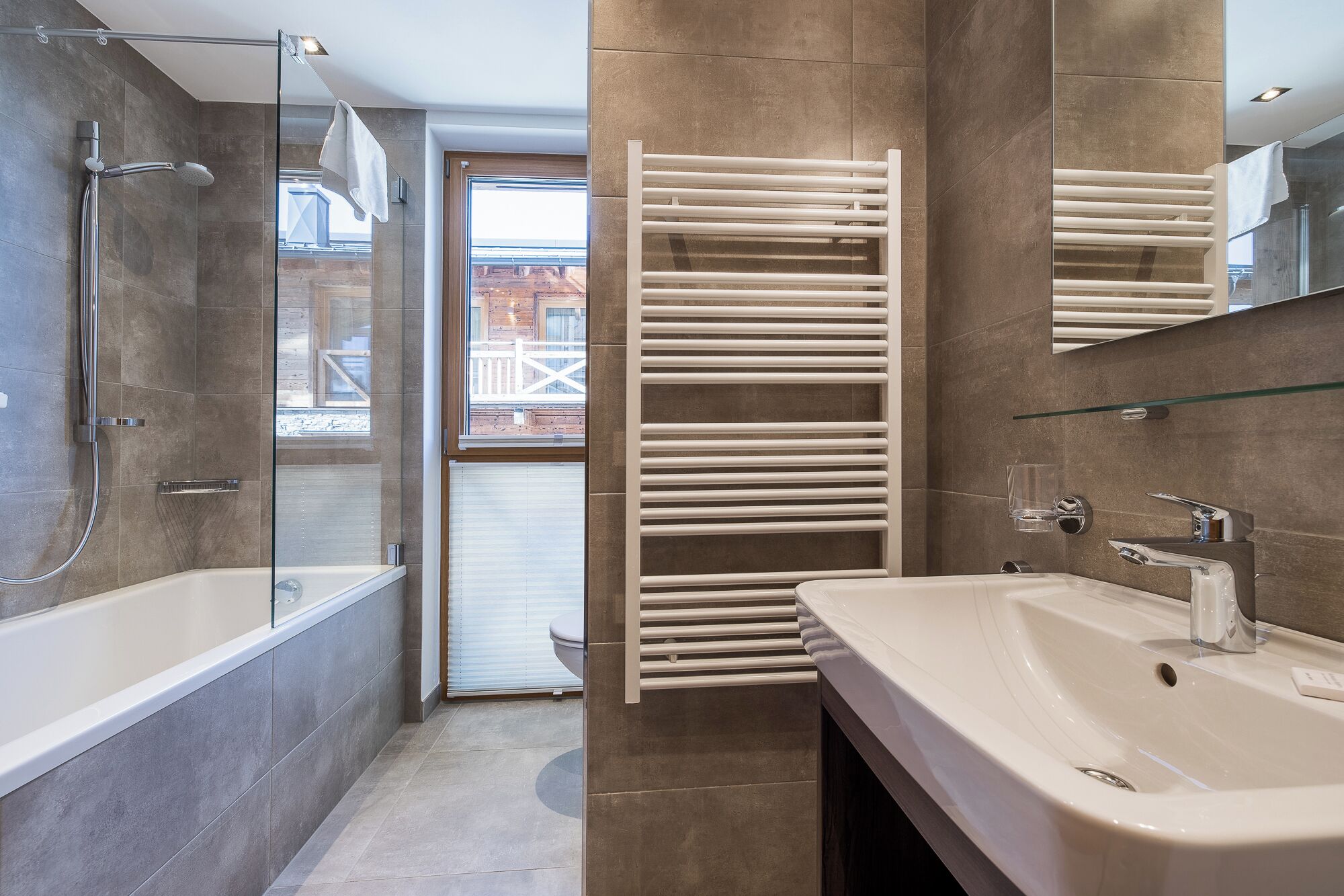 Un baño moderno con ducha envuelta en vidrio, toallero empotrado y un lavamanos grande.