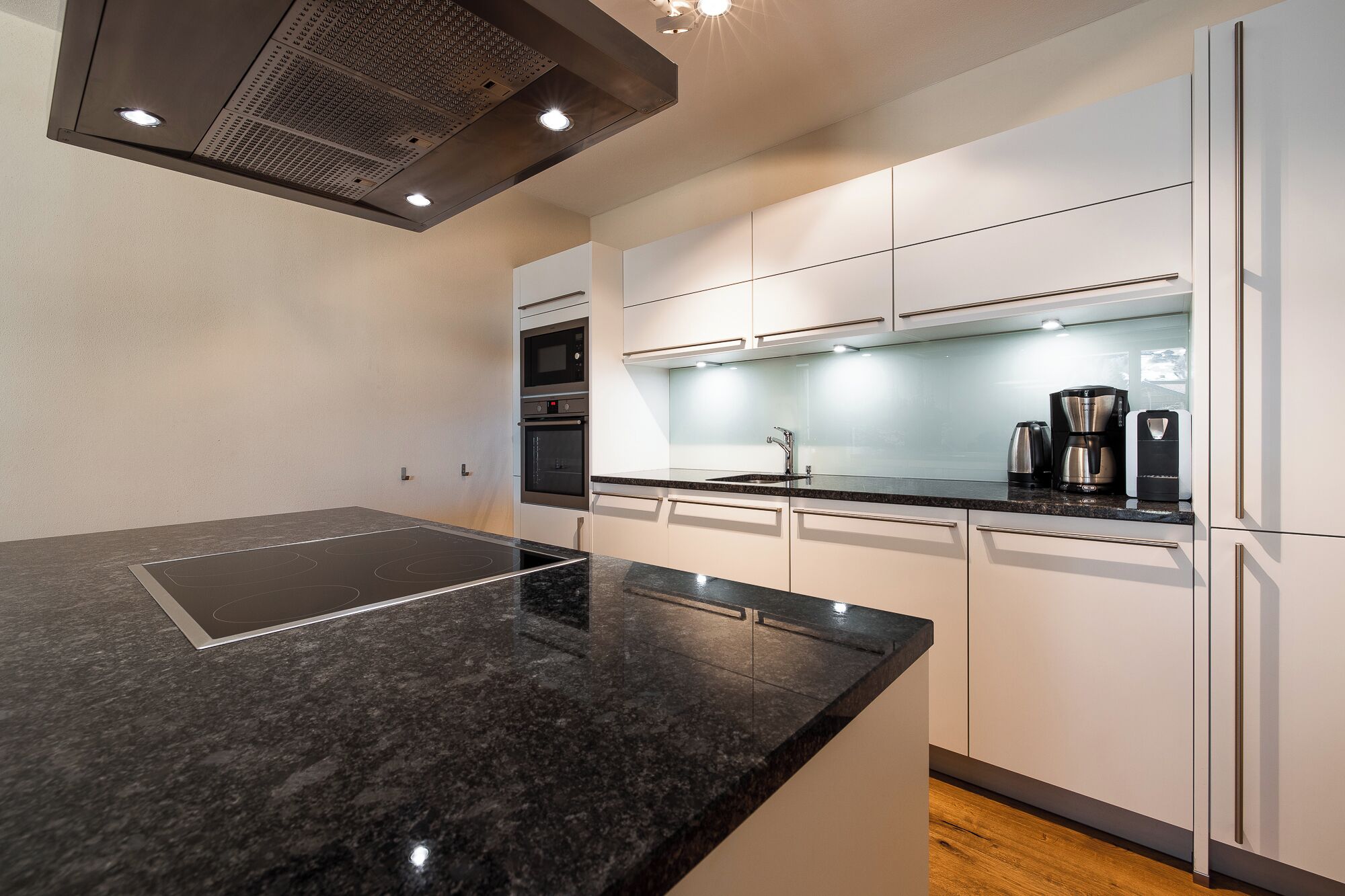 A modern kitchen with a black countertop, white cabinets, and stainless steel appliances including a microwave, oven, and coffee maker.