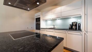 A modern kitchen with a black countertop, white cabinets, and stainless steel appliances including a microwave, oven, and coffee maker.