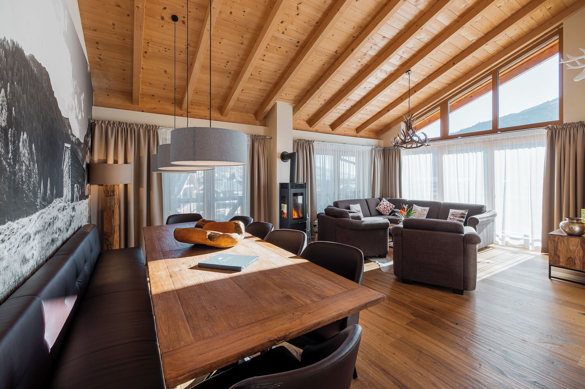 Een ruime woonkamer met een houten plafond, een eettafel, een bank en een open haard.