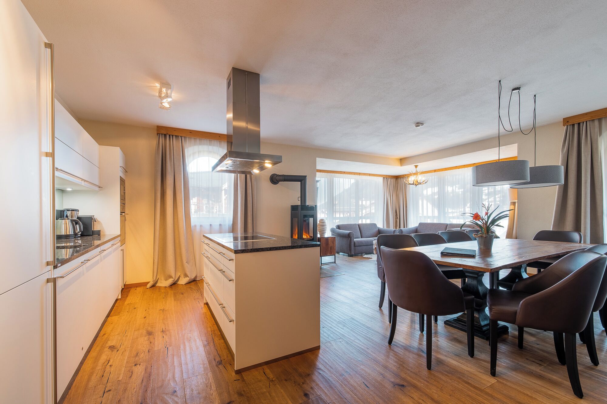 Una cocina moderna con una isla central, un área de comedor con mesa y sillas de madera, y un espacio de sala de estar con sofá y chimenea.