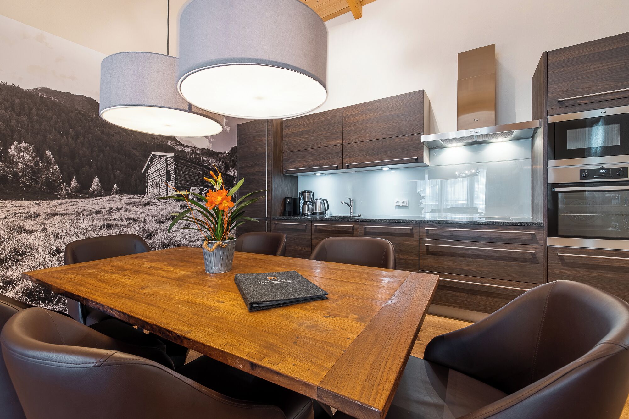 Eine moderne Küche mit dunklen Holzschränken, Edelstahlgeräten und einem Essbereich mit Holztisch und Stühlen.