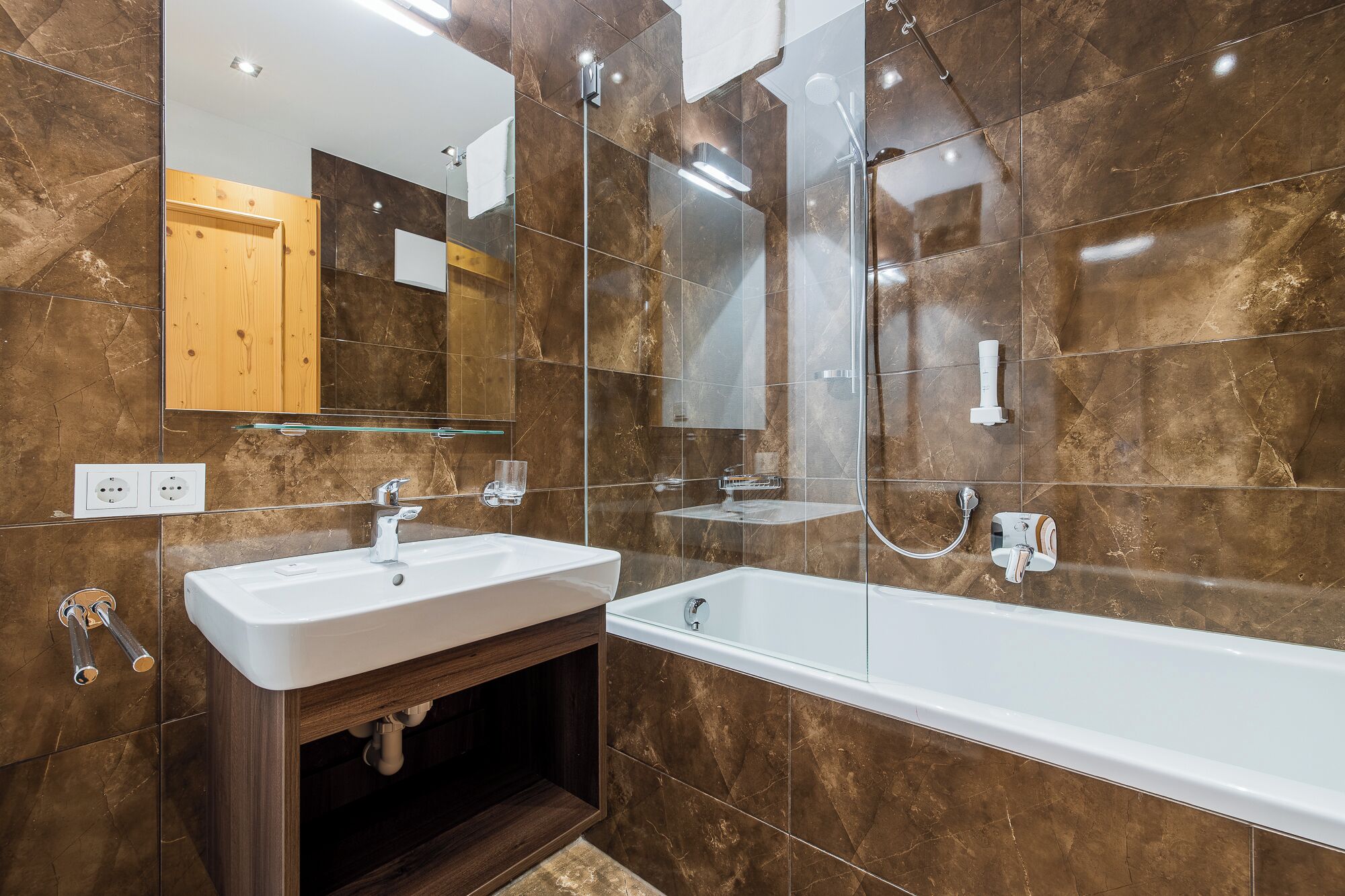 Un baño moderno con bañera, dos lavamanos, cabina de ducha de vidrio y un mueble de madera.
