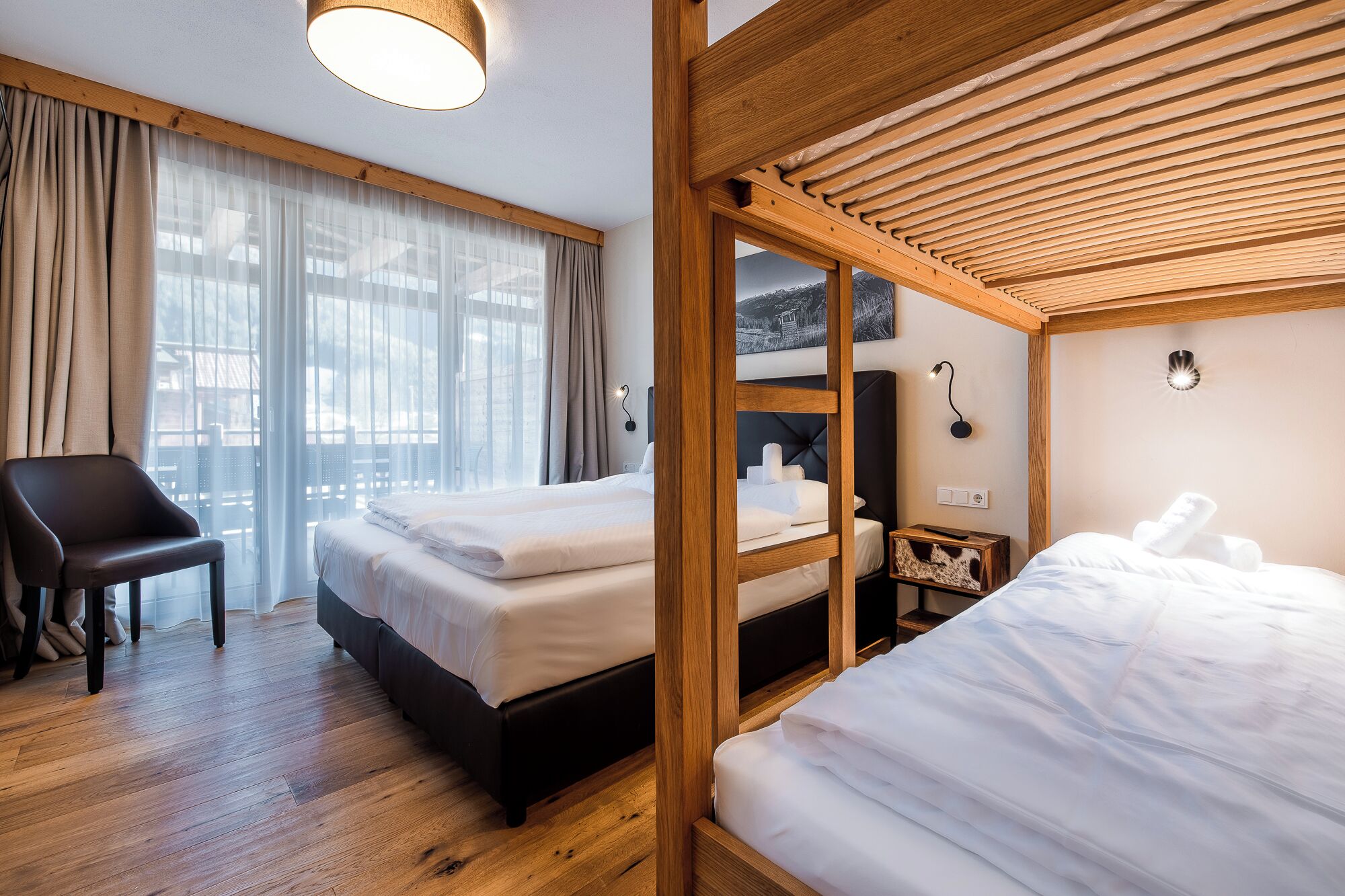 A hotel room with two beds, a wooden ceiling, a chair, and a large window with curtains.