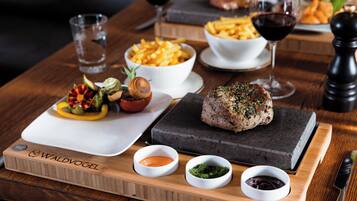 A wooden serving board with a steak, vegetables, and sauces.