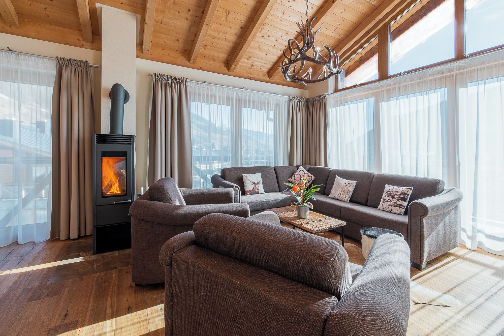 A cozy living room with a fireplace, wooden ceiling, and large windows.
