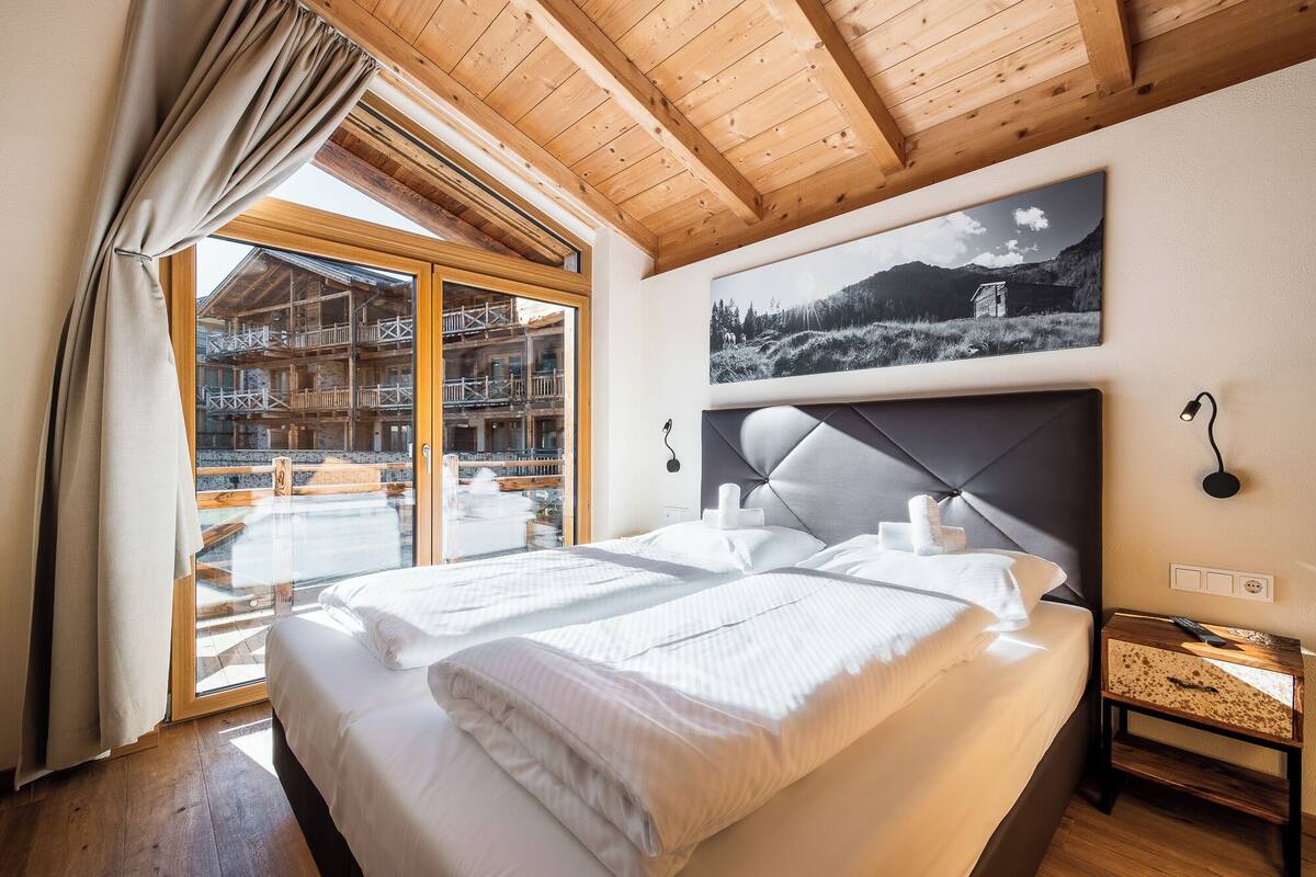 Habitación de hotel con una cama grande, techo de madera y vistas a un paisaje montañoso.