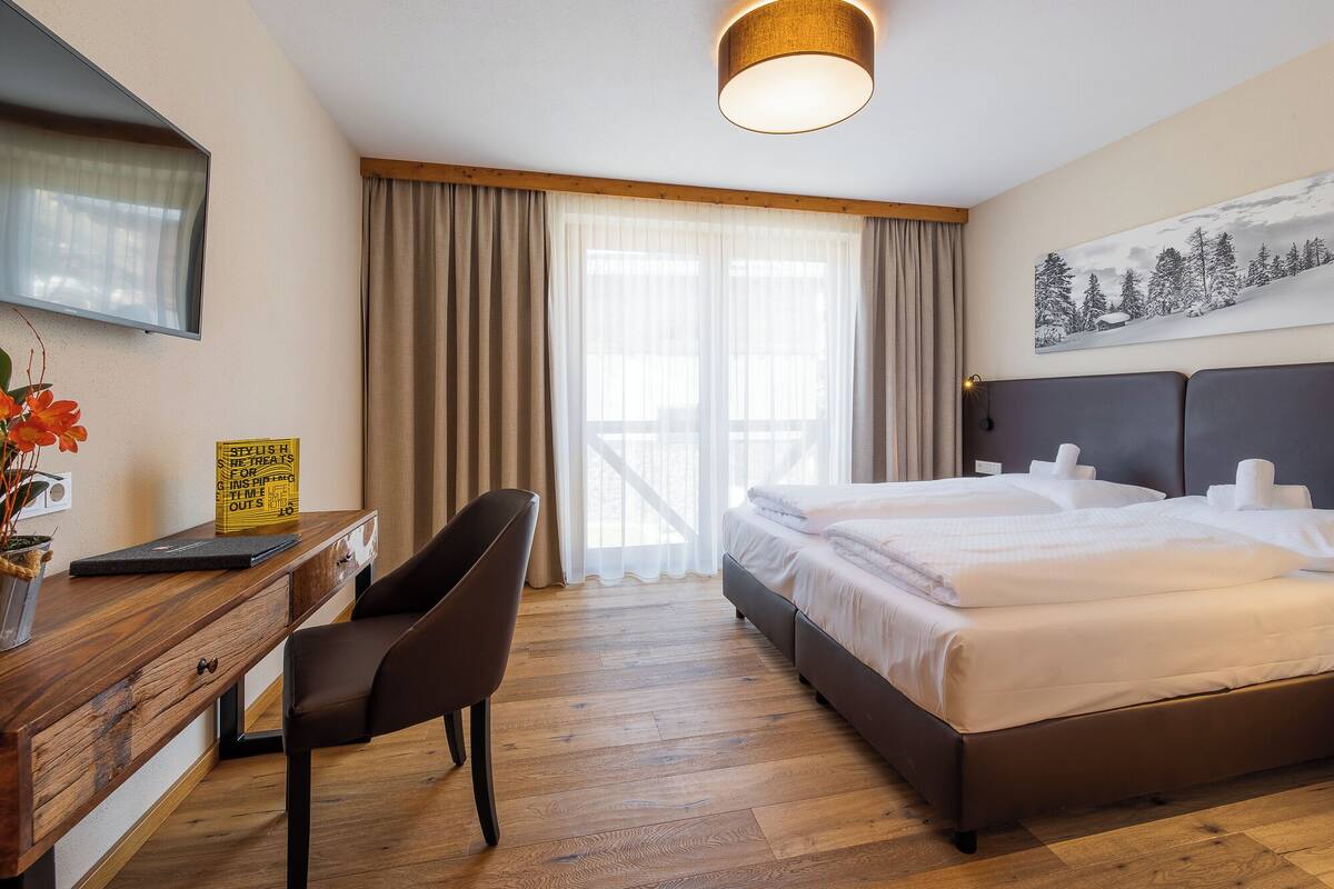 Habitación de hotel con cama, escritorio con silla, televisor y ventana con cortinas.