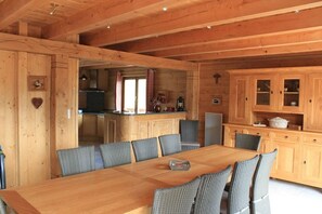 Interior de una cabaña de madera con una mesa de comedor y sillas, una zona de cocina y una chimenea acogedora.