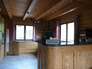 Une cuisine rustique, aménagée dans une cabane en bois, avec un îlot central, une fenêtre offrant une belle vue et un panneau indiquant « MOUCHOIRS » sur l’îlot.