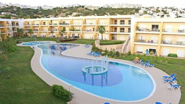 A resort with a large swimming pool, multiple lounge areas with sun loungers, and a backdrop of multi-story buildings. - Apartment Amelo, fantastic clean apartment near marina (Albufeira)