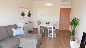 A living room with a sofa, a dining table with chairs, a small kitchen area, and a door. - Apartment Amelo, fantastic clean apartment near marina (Albufeira)
