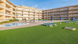 Un hôtel à plusieurs étages doté d’une piscine, d’une pelouse artificielle et de chaises longues.