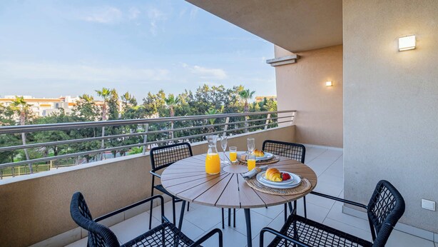 Un balcon avec une table ronde mise pour le petit-déjeuner, comprenant des croissants, des fruits et du jus d’orange.
