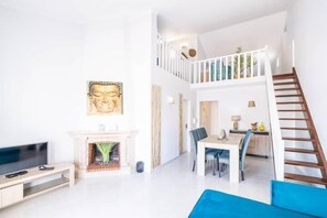 A bright living room with a fireplace, a dining area, and a staircase leading to an upper level.